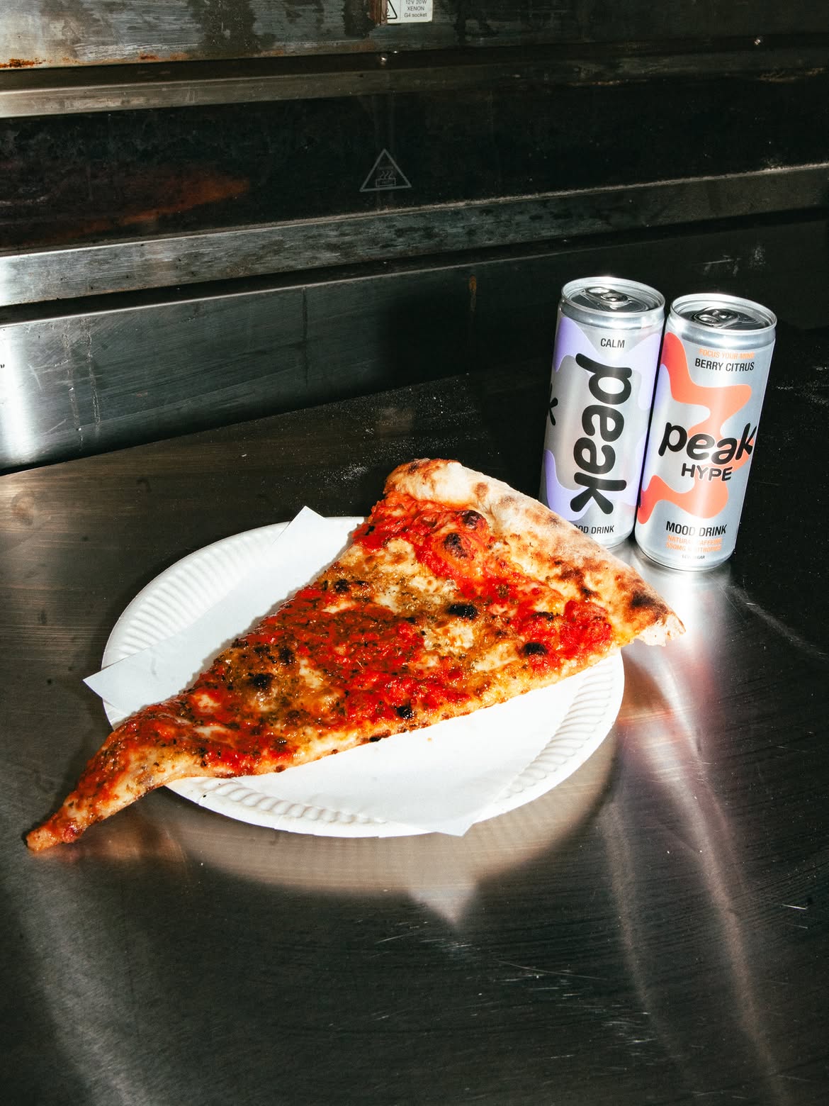 A slice of pizza with cans of Peak Calm and Peak Hype