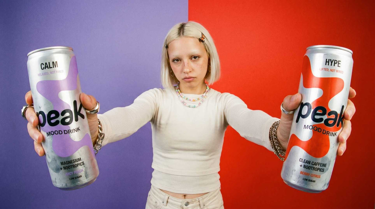 A woman holding out a can of Peak Calm and a can of Peak Hype