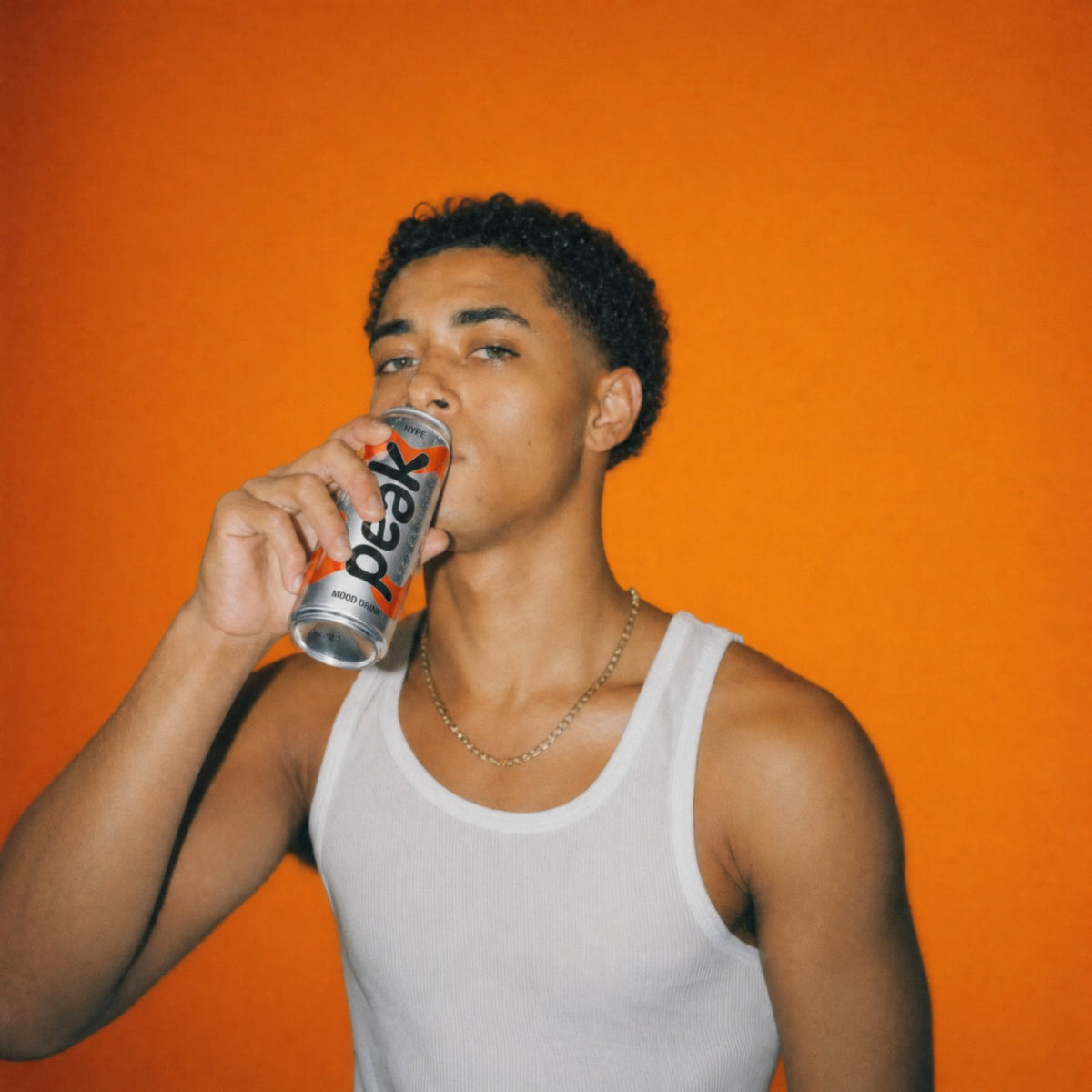 A man drinking a can of Peak Hype on an orange background